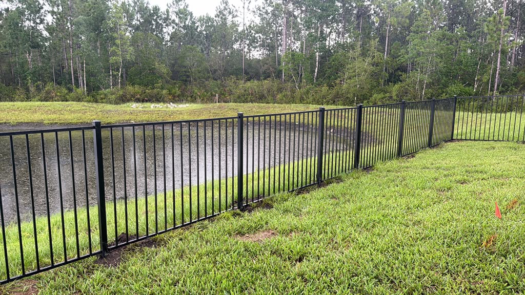 Black metal fence following a backyard beside a pond